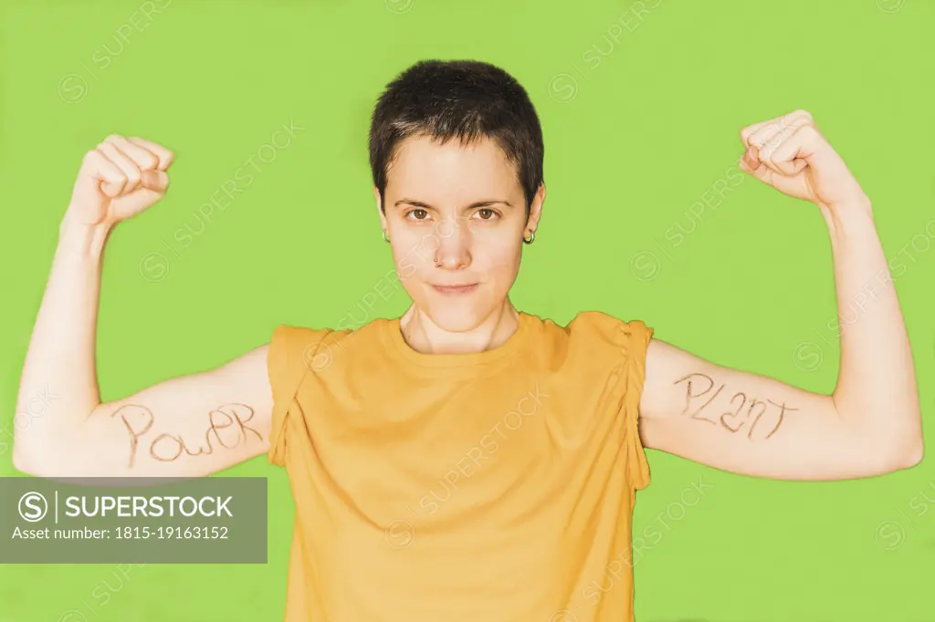Woman with short hair flexing muscles against green background