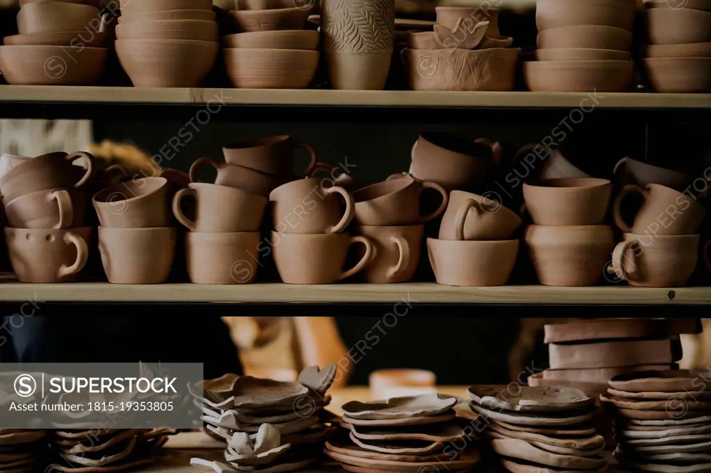 Handmade ceramic bowls with cups and plates on shelf in workshop