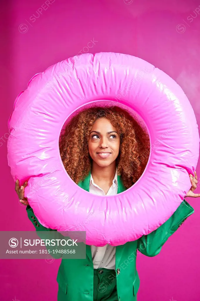 Smiling businesswoman looking though inflatable ring against pink background