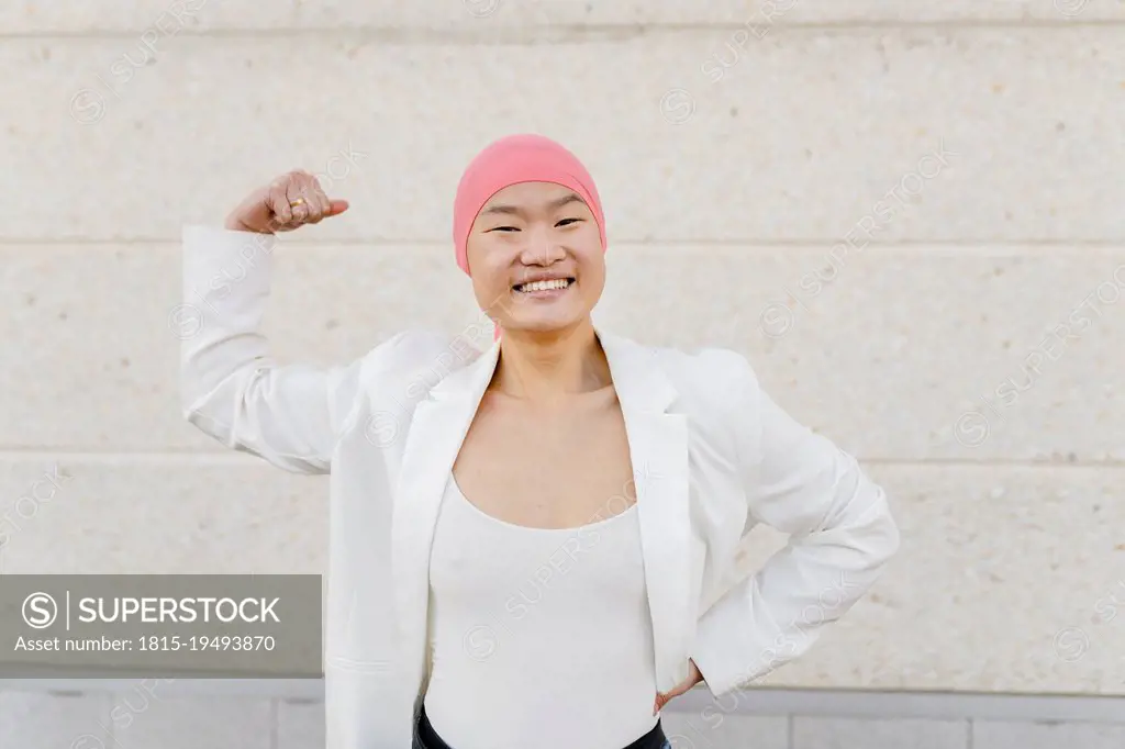 Smiling woman wearing pink bandana showing bicep in front of white wall