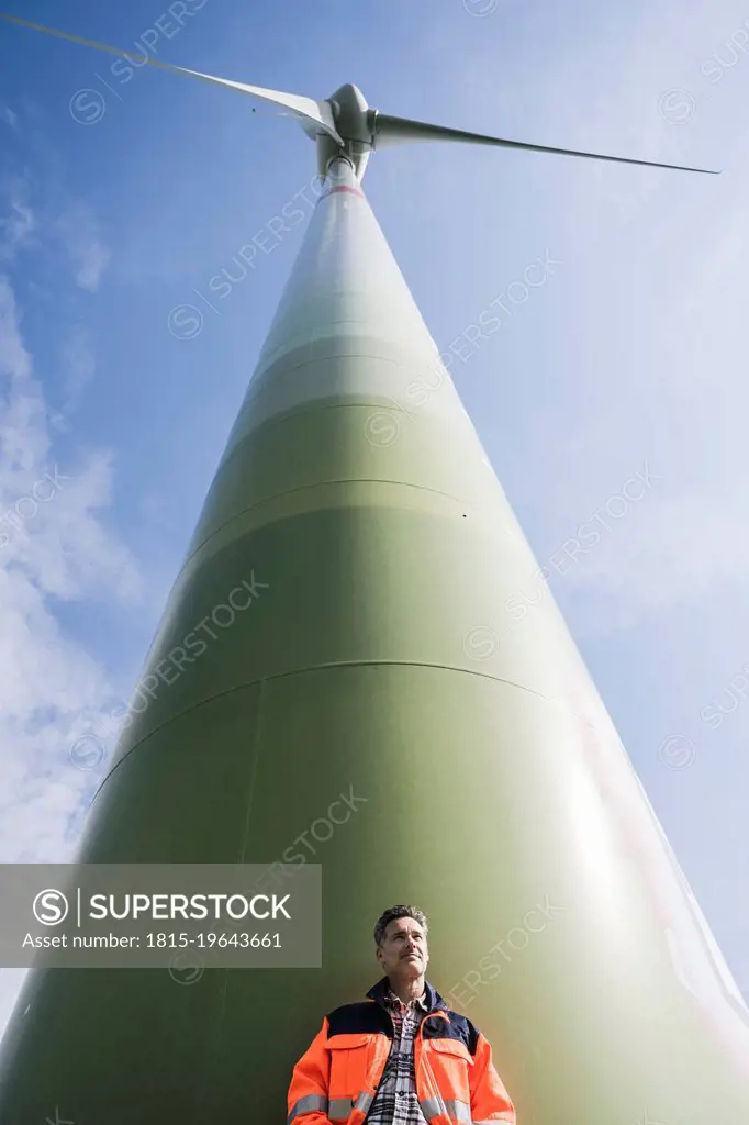 Engineer standing in front of tall wind turbine on sunny day
