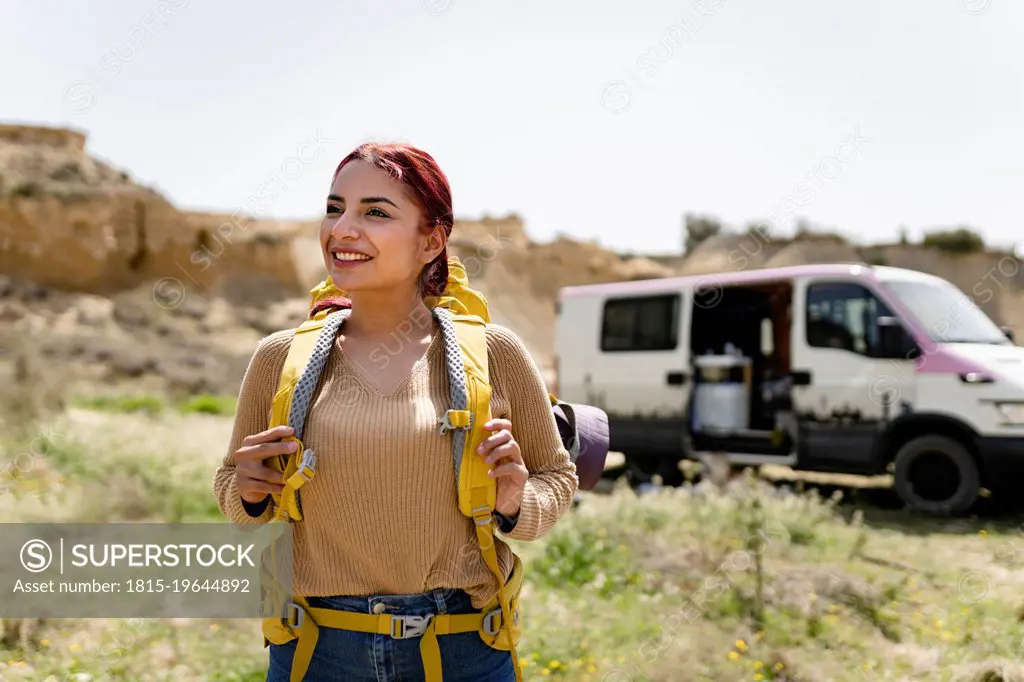 Smiling woman with backpack standing in front of motor home on sunny day