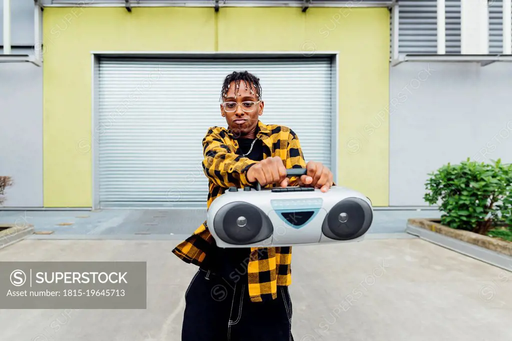 Young man wearing eyeglasses dancing with boom box in front of shutter