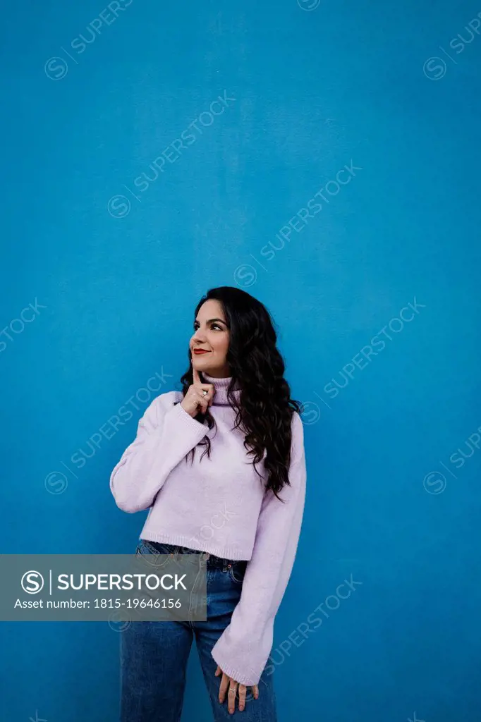 Thoughtful woman standing in front of blue wall
