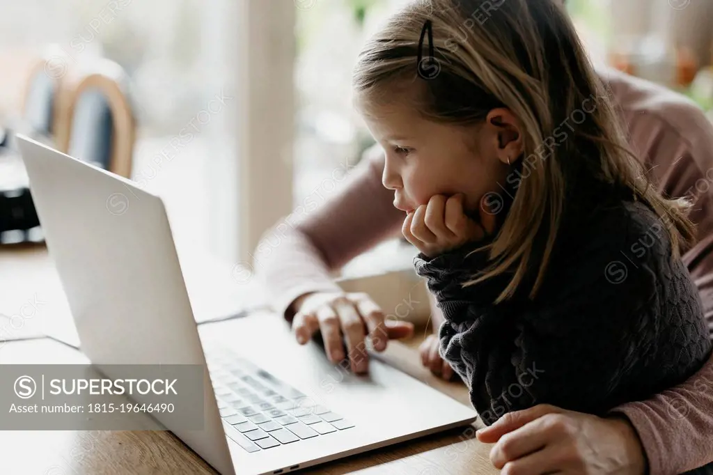Girl with hand on chin looking at laptop sitting with mother