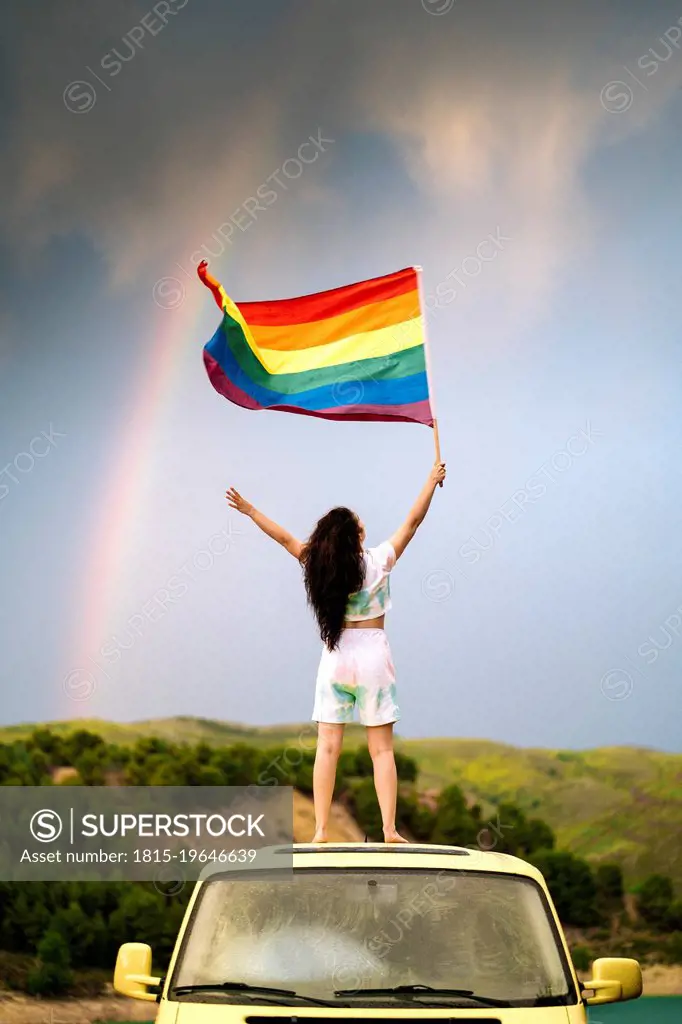 Young woman holding rainbow flag standing on van