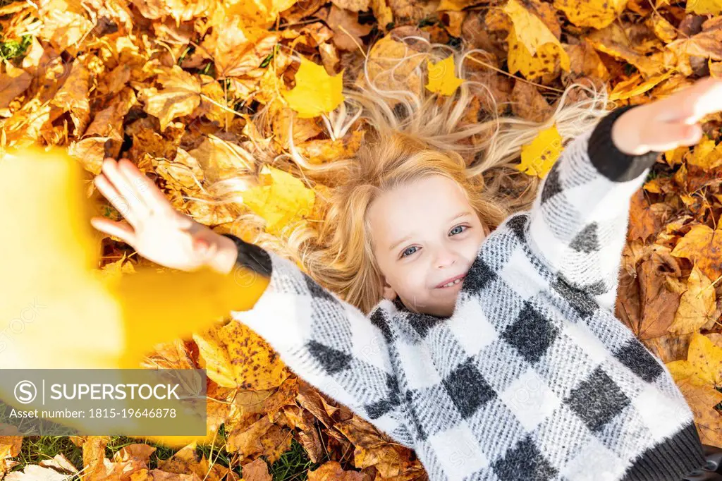 Playful girl lying on autumn leaves at park