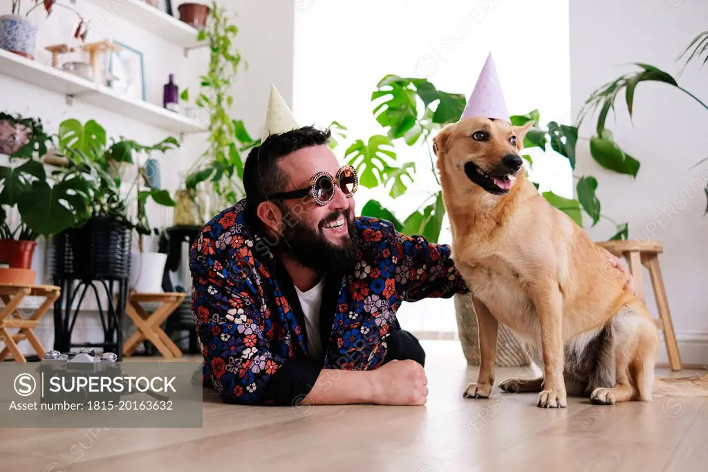 Happy man wearing sunglasses lying by pet dog at home