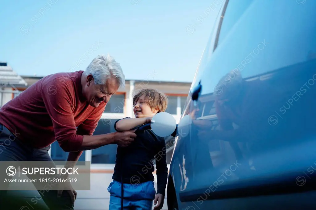 Happy senior man and grandson charging electric car