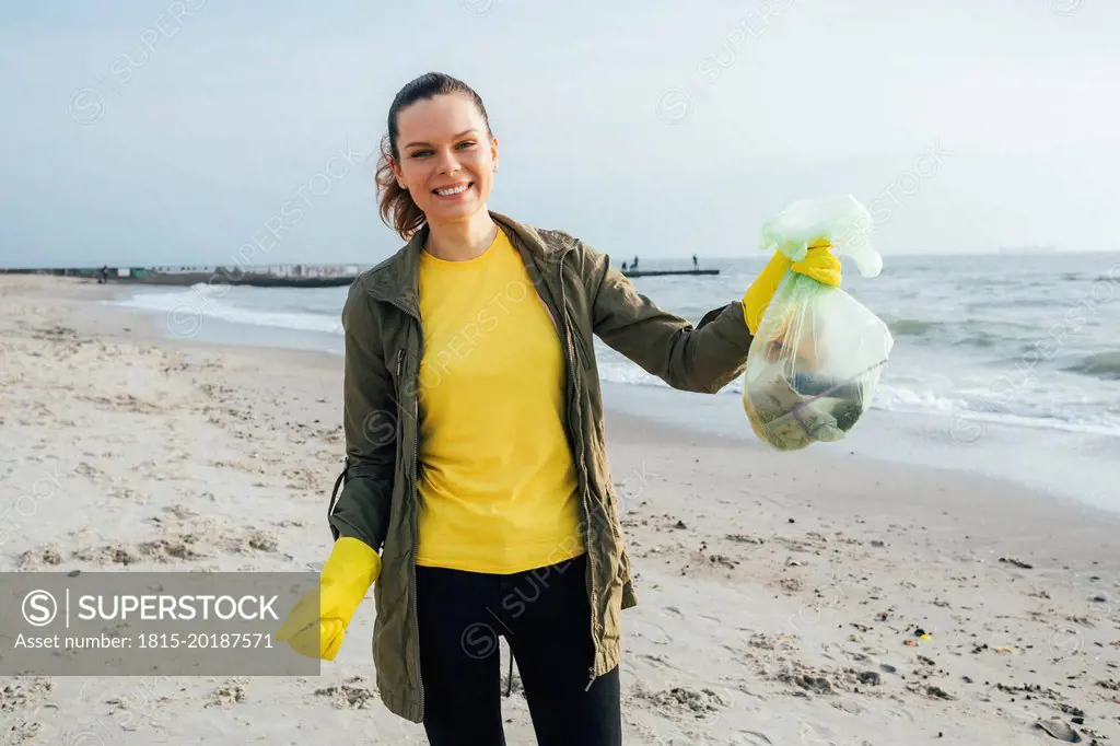 Happy volunteer showing garbage bag at beach