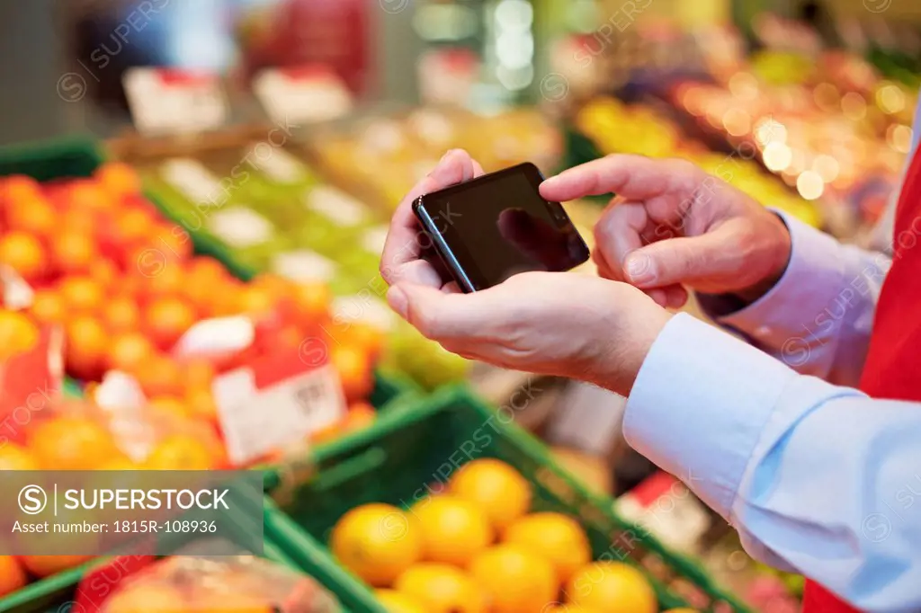 Germany, Cologne, Mature man using smart phone in supermarket