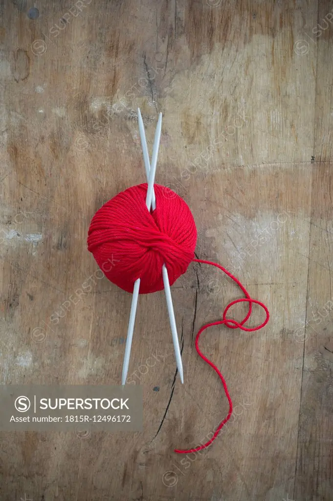 Red ball of wool and knitting needles on wood
