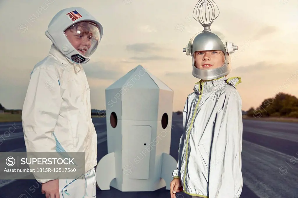 Two boys dressed up as spacemen standing at cardboard rocket