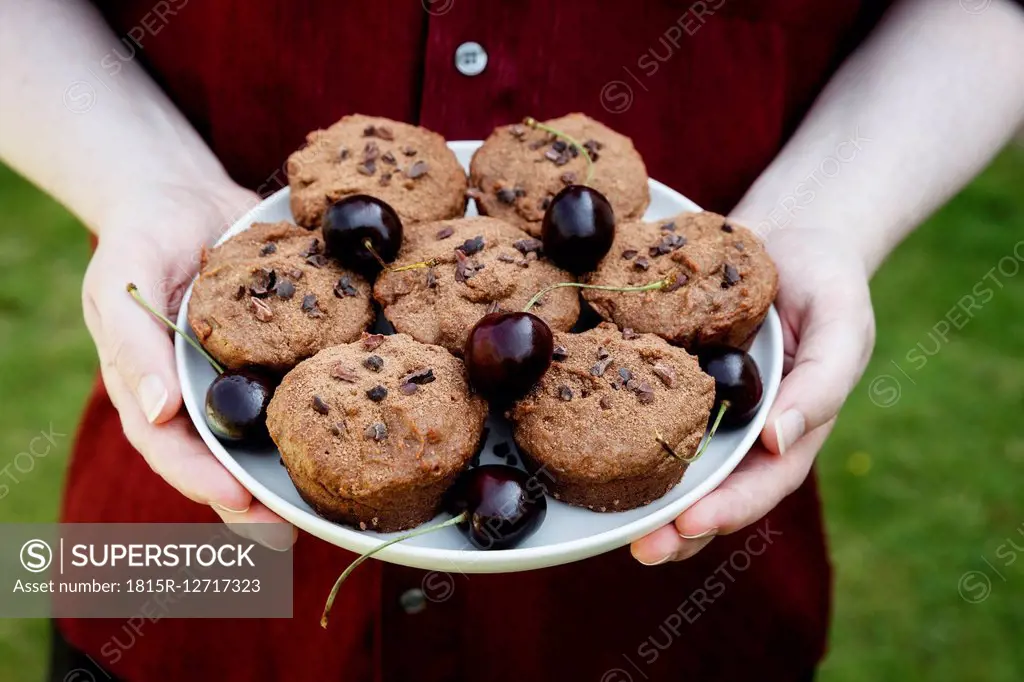 Man holding plate with vegan chocolate muffins with cherries