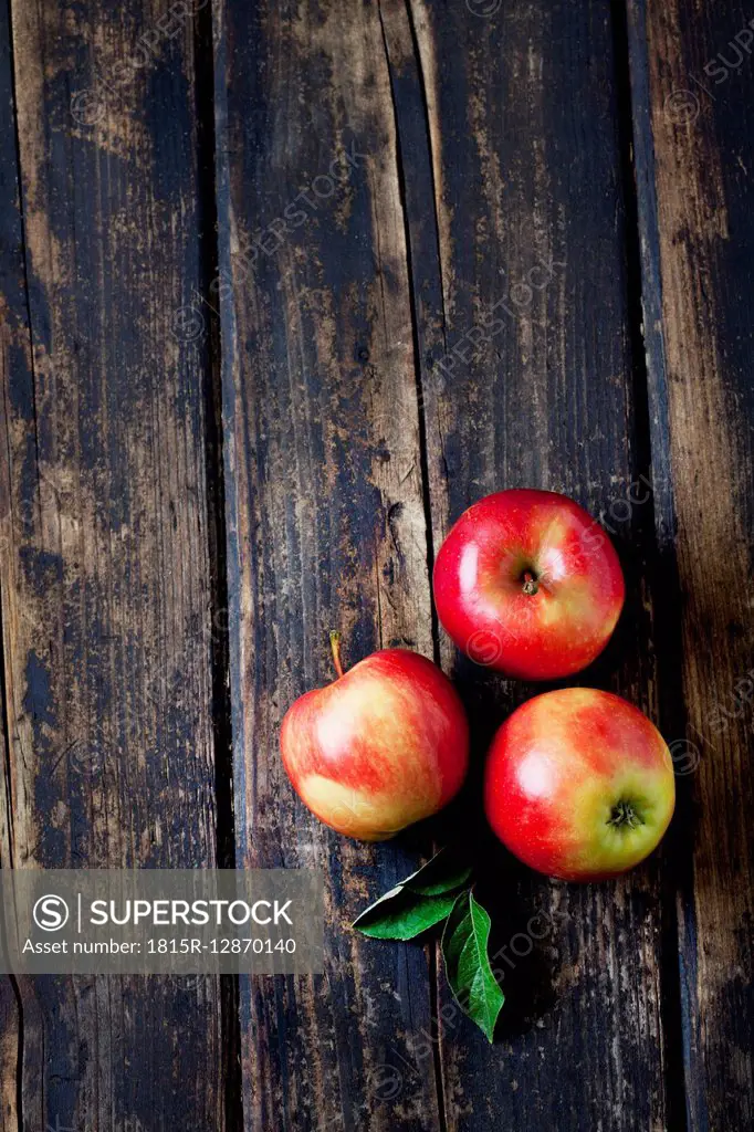 Three red apples and leaves on dark wood