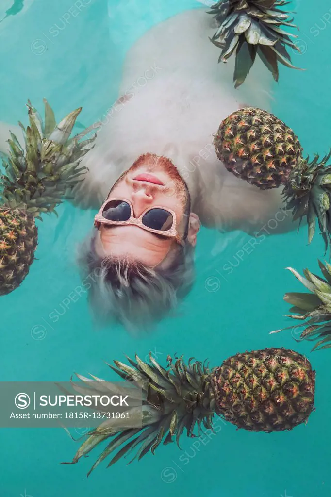 Young man in swiming pool surrounded by pineapples