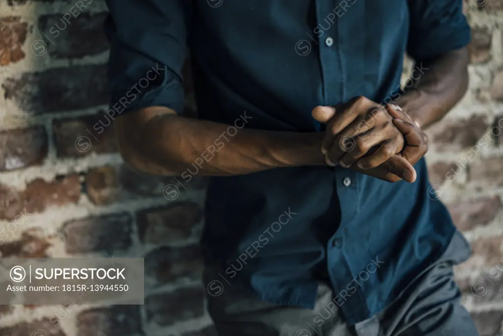 Hands of man leaning against brick wall