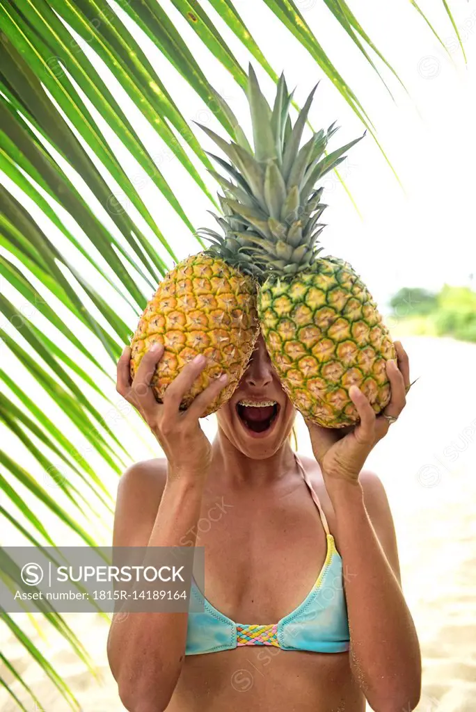 Young woman holding two pineapples at palm tree