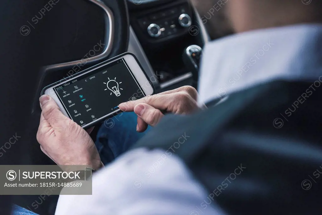Man in car adjusting smart home device via smartphone