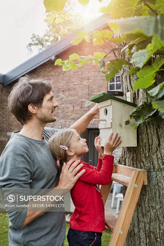 Father and daughter hanging up nest box in garden