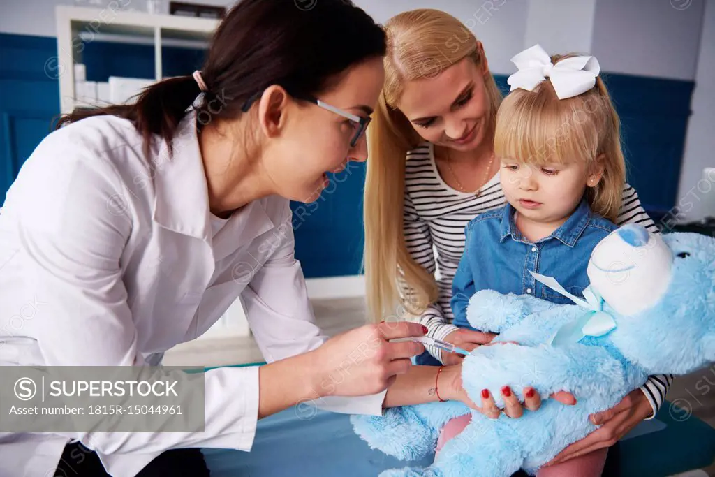 Doctor and girl with mother vaccinating teddy in medical practice