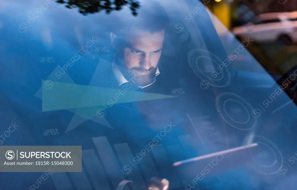Businessman with tablet in car at night surrounded by data