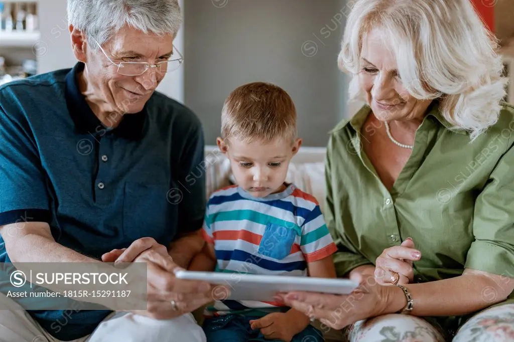 Grandparents and grandson at home sitting on couch sharing tablet