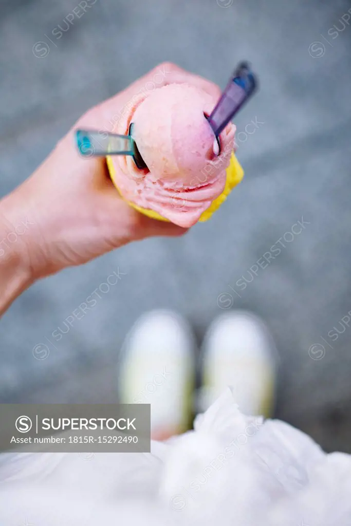 Woman's hand holding ice cream cone with two scoops and spoons