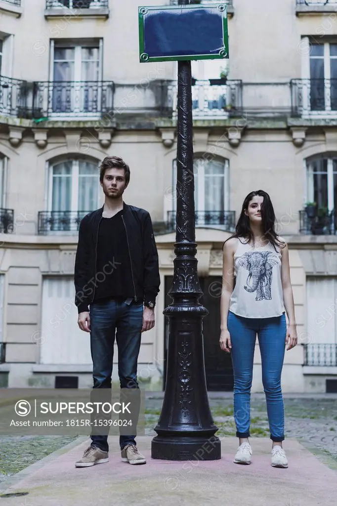 France, Paris, young couple standing at lamp post in front of urban building