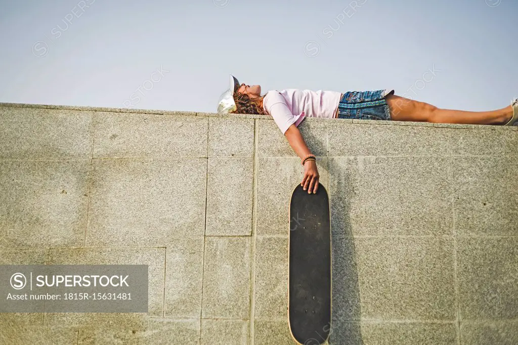 Girl with skateboard lying on wall