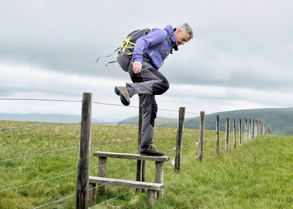 UK, Lake District, Longsleddale valley, mature man with backpack crossing pasture fence