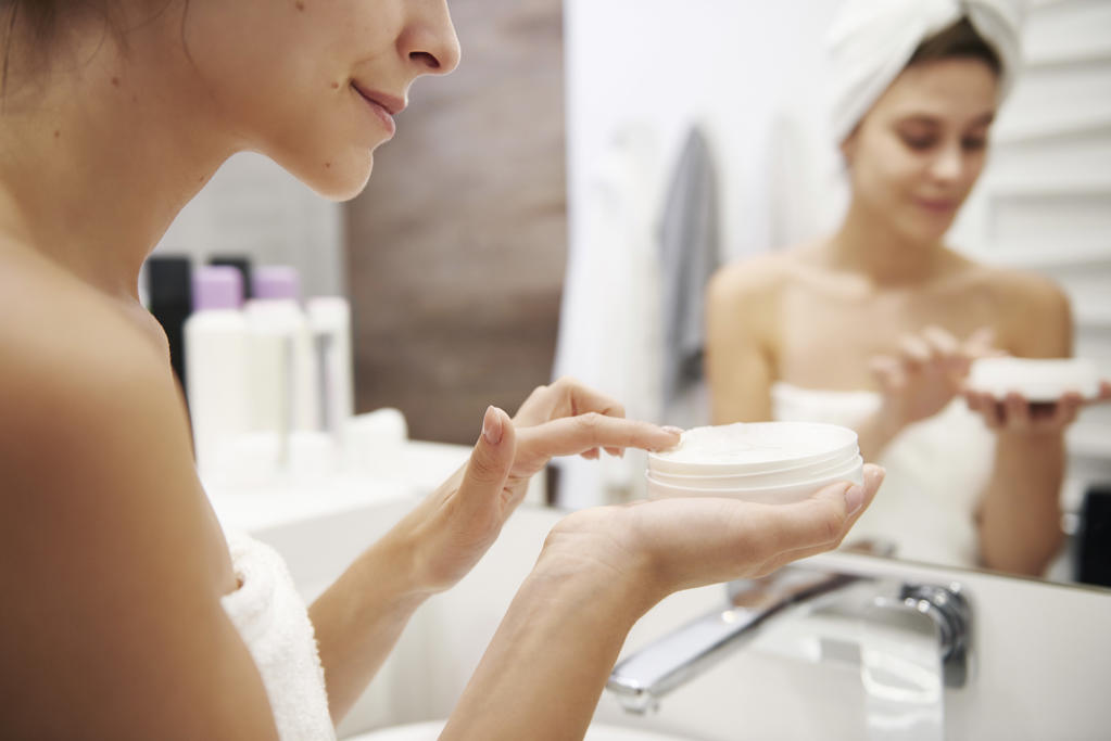 Young woman applying moisturizer in bathroom, partial view