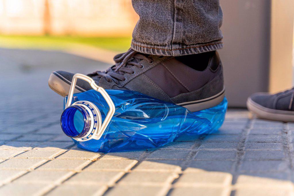 Close-up of man's feet sqashing plastic bottle for recycling