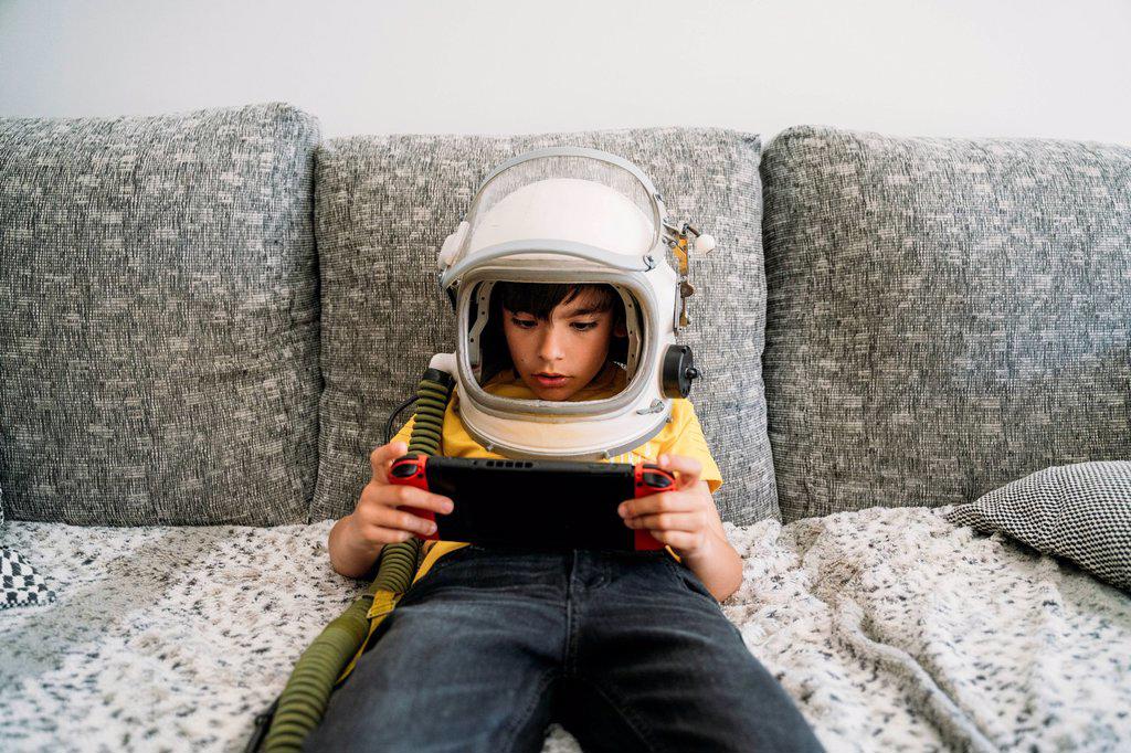 Boy playing video game on a games console, wearing space hat