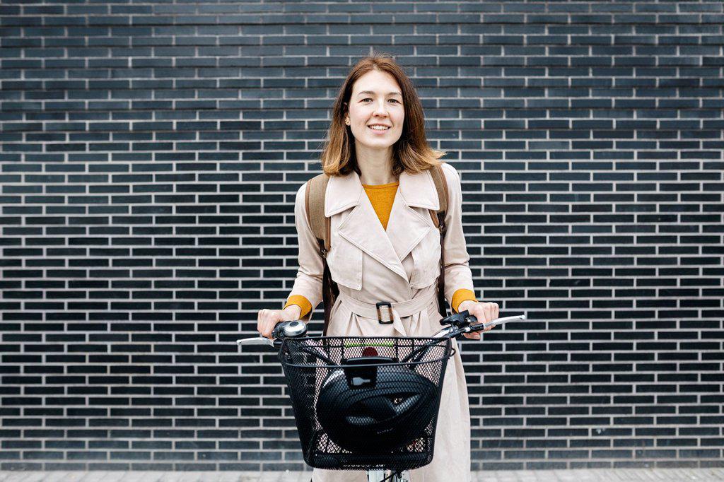 Portrait of smiling woman with e-bike at a brick wall