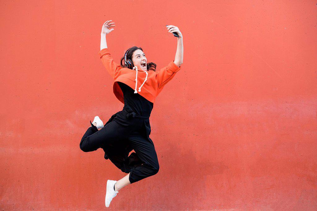 Young contemporary dancer jumping and using smartphone in front of a red wall