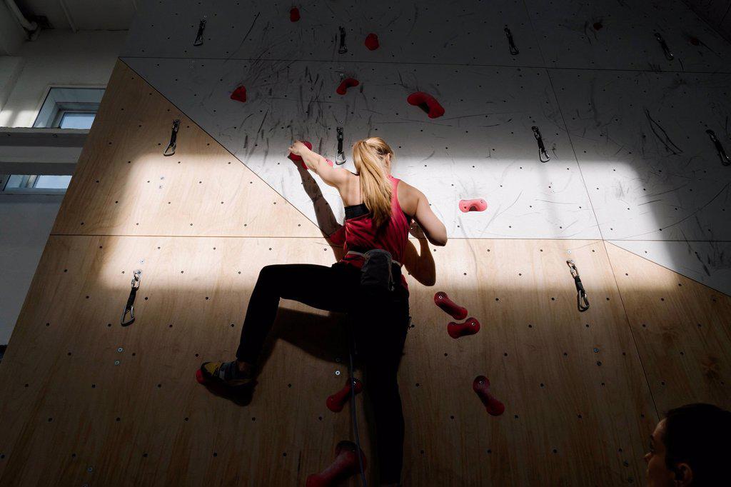 Woman climbing on the wall in climbing gym with sunlight and shadow