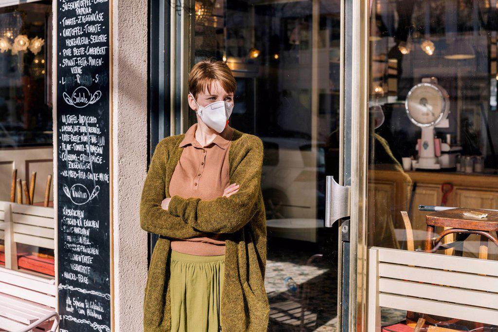 Woman wearing mask standing in front of her closed restaurant