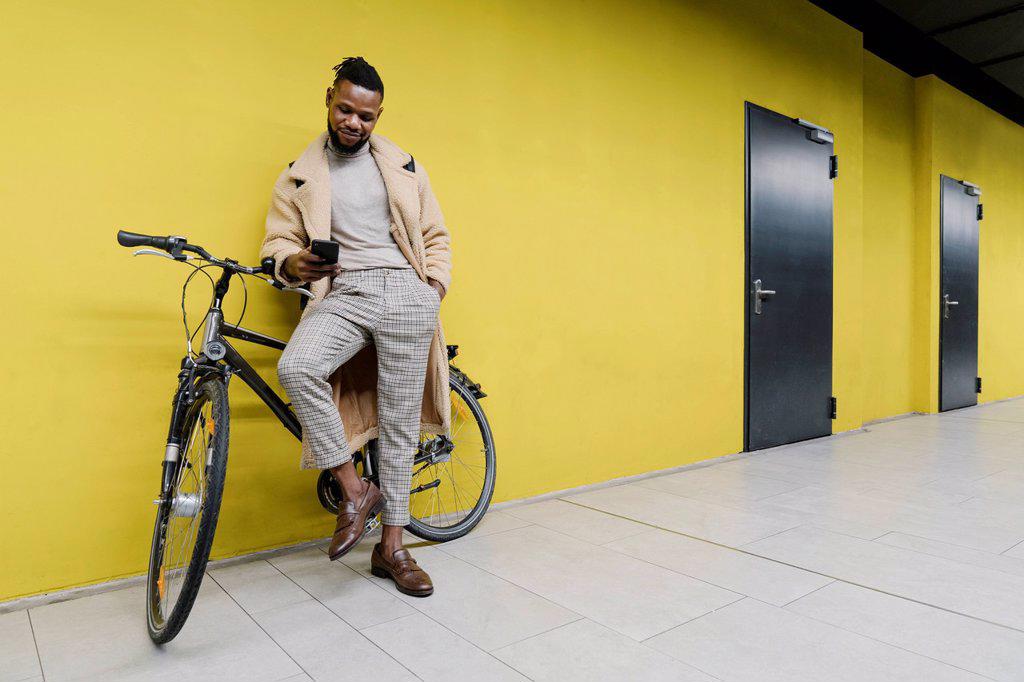 Stylish man with a bicycle and smartphone at a yellow wall