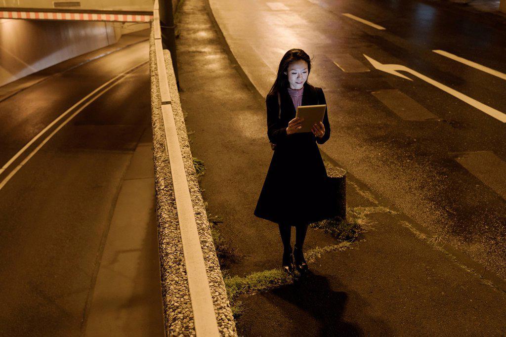 Young woman using tablet in the city at night, Frankfurt, Germany