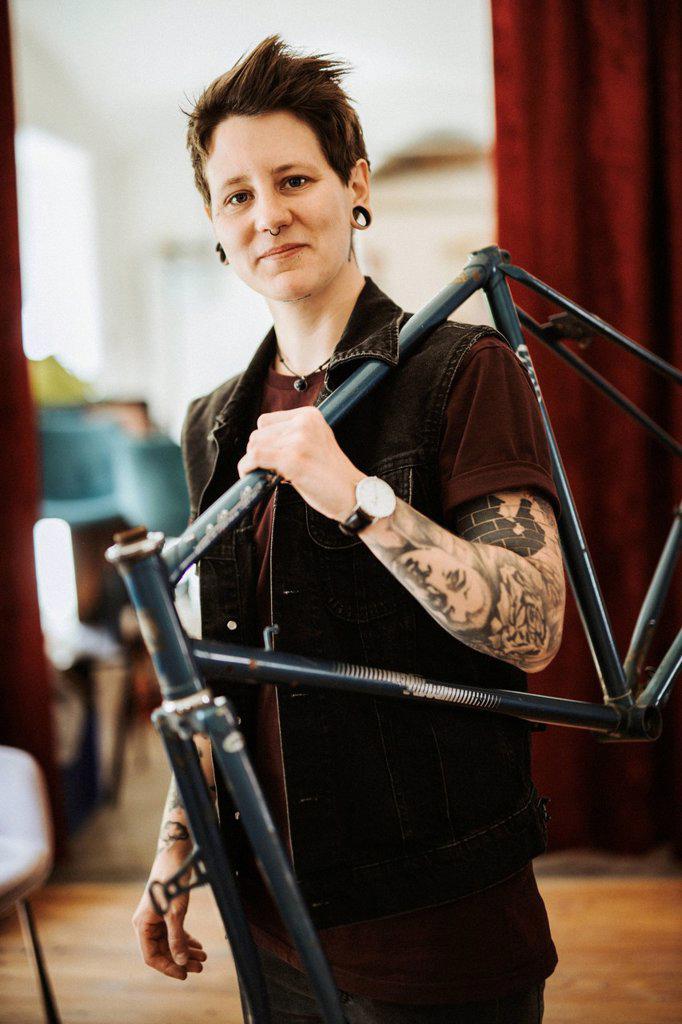 Portrait of pierced and tattooed woman with bicycle frame on her shoulder