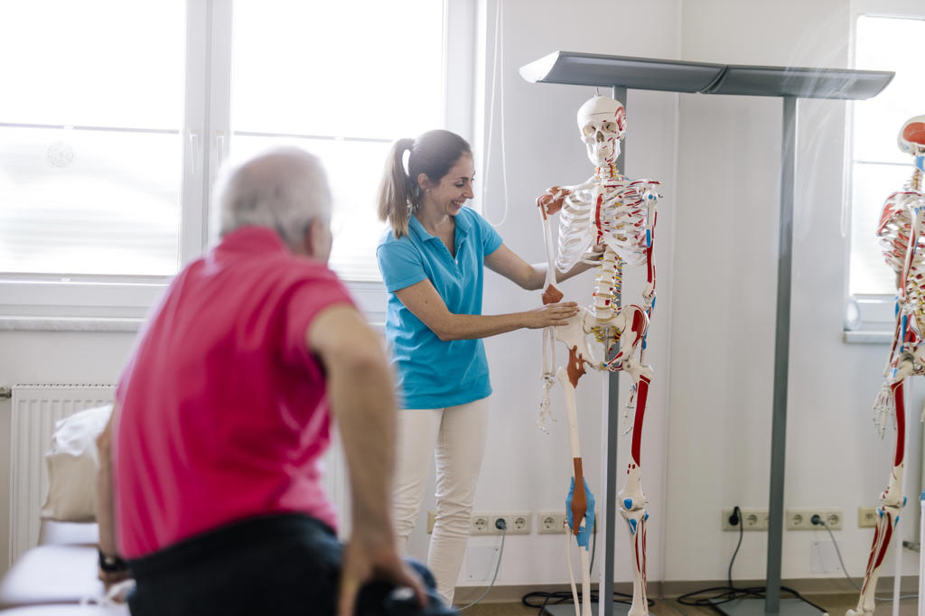 Female physiotherapist explaining treatment to patient, using skeleton