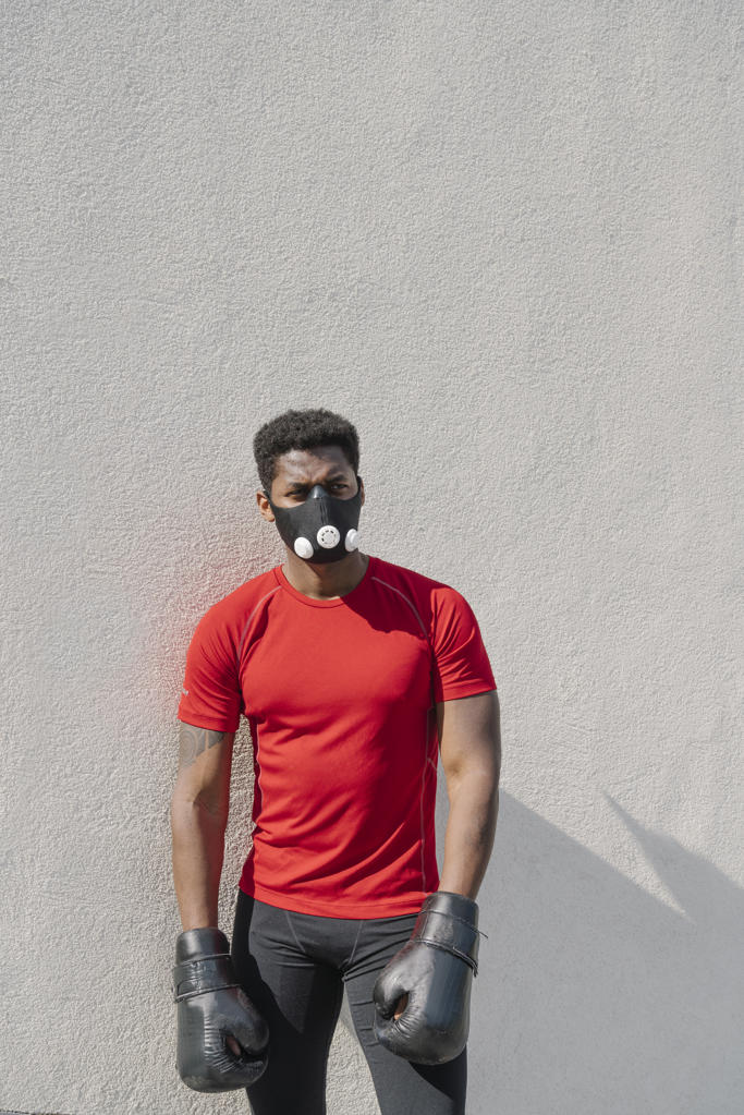 Portrait of a sportsman wearing face mask and boxing gloves at a wall