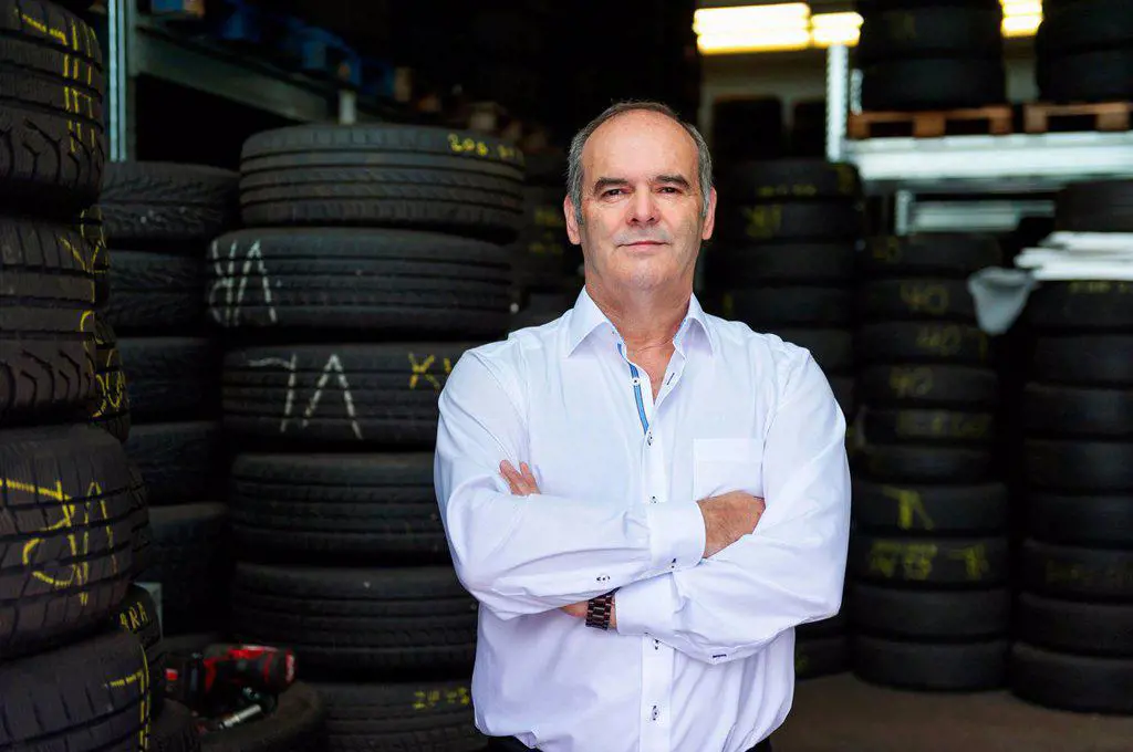 Portrait of confident senior male owner standing with arms crossed against tire at store