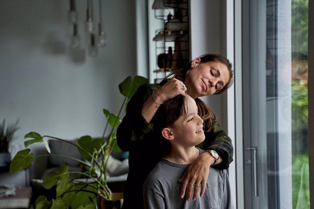 Loving woman standing with son looking through window at home