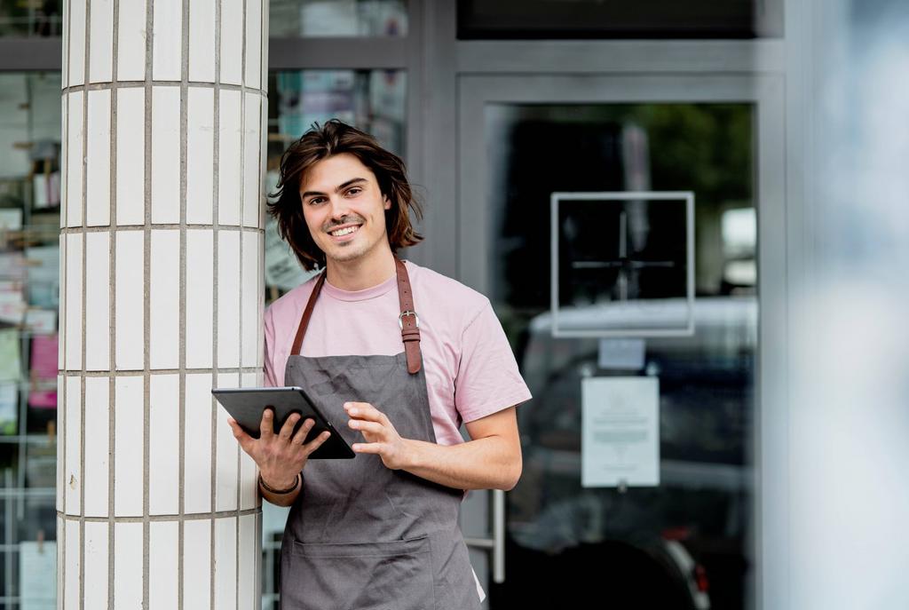 Smiling owner using digital tablet while standing by column against cafe