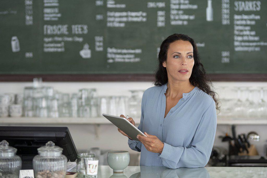 Female owner using digital tablet looking away while standing by counter in cafe