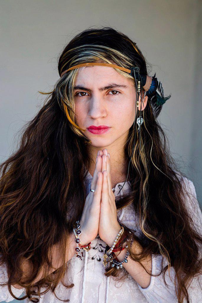 Close-up of hippie woman standing in prayer pose against wall