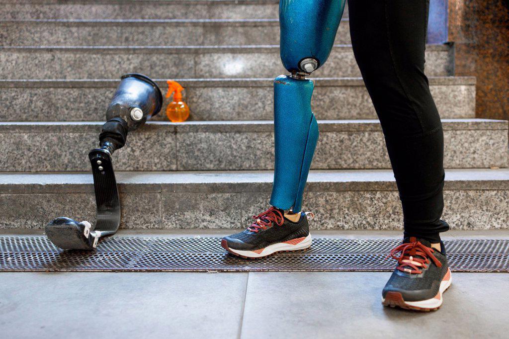 Young sportswoman with prosthetic leg standing by artificial limb on steps