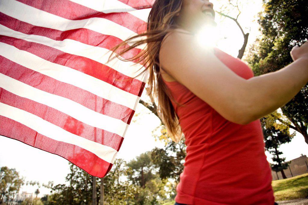 Young woman running in park while holding American flag during sunny day